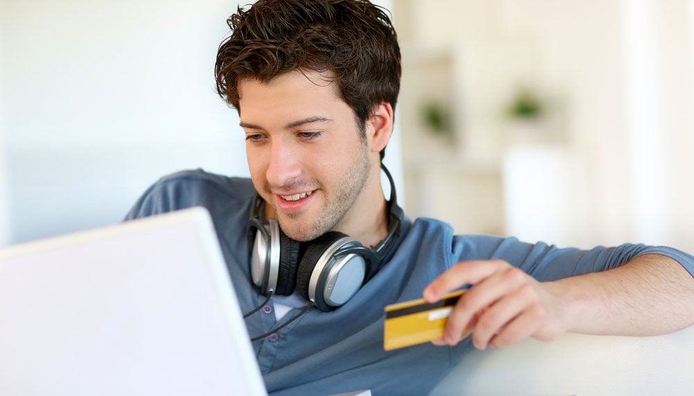 Young man buying a new home online with laptop and credit card in his hand