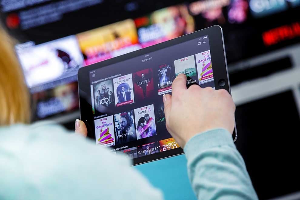 Woman Holding a touch pad and switching channels on France Netflix HomePage with TV set on background